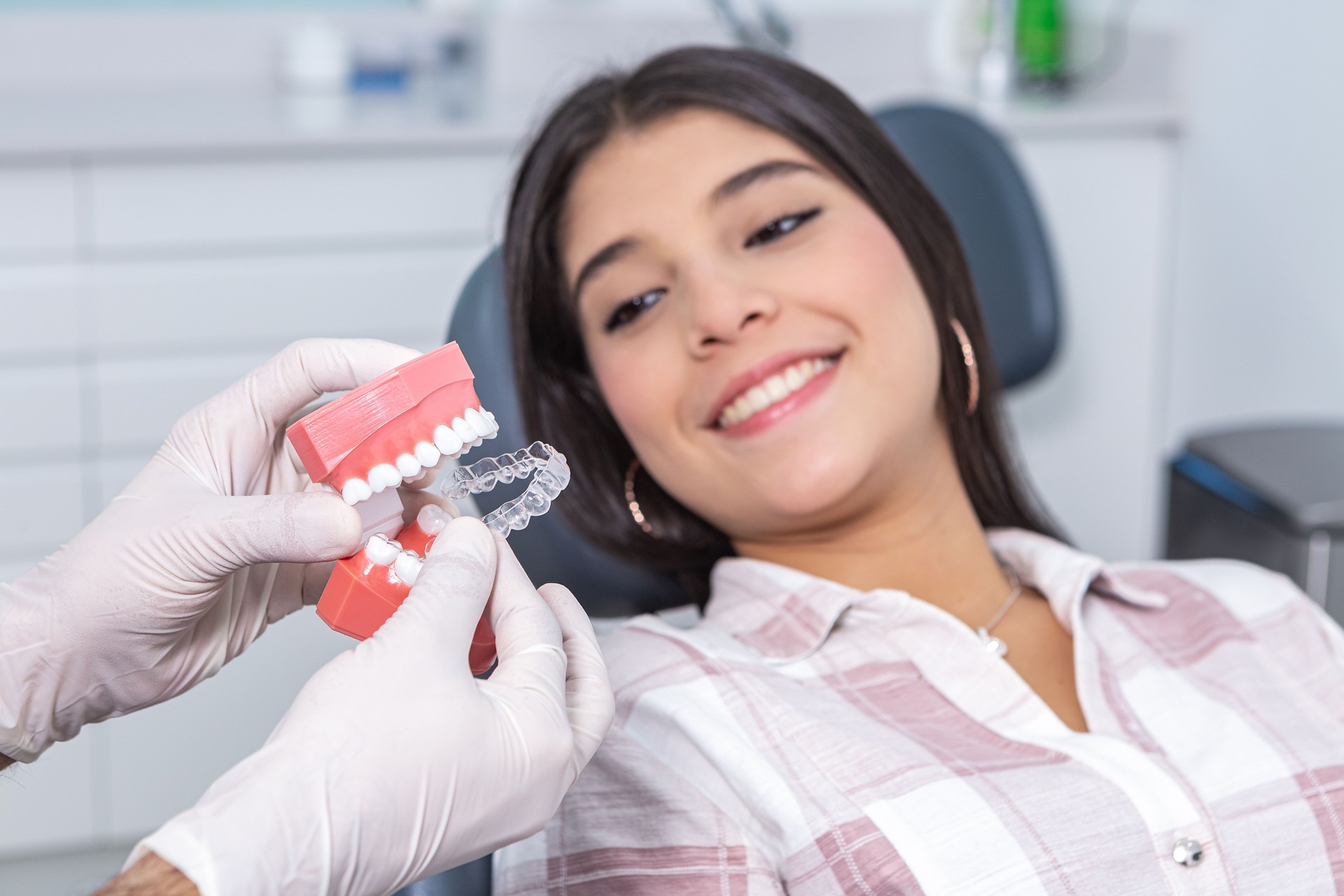 Crop stomatologist showing vacuum formed retainer to happy ethnic female patient